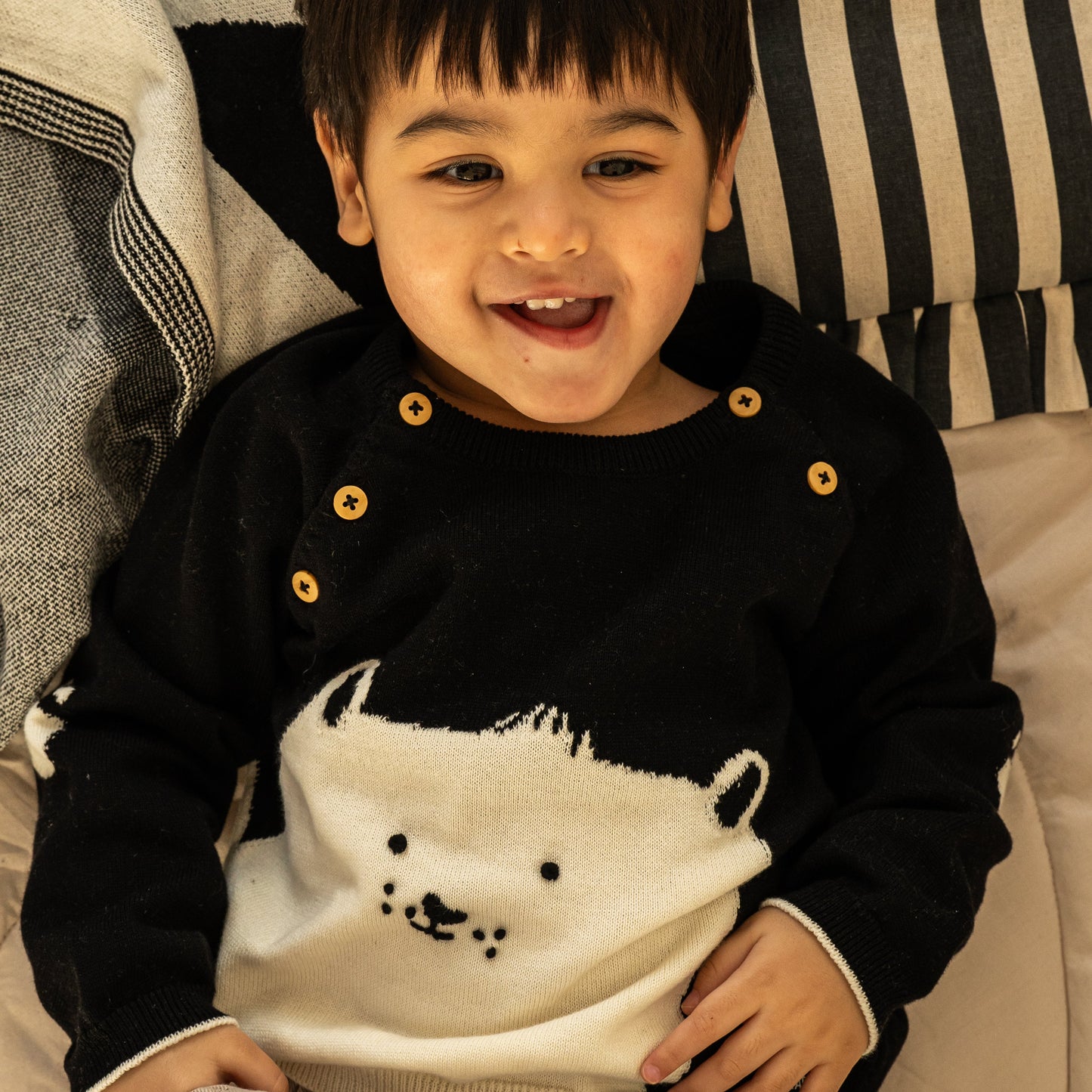A young child wearing a black and white knit sweater with a polar bear design, lying on a striped cushion.
