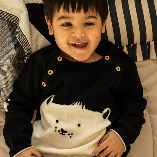 A young child wearing a black and white knit sweater with a polar bear design, lying on a striped cushion.